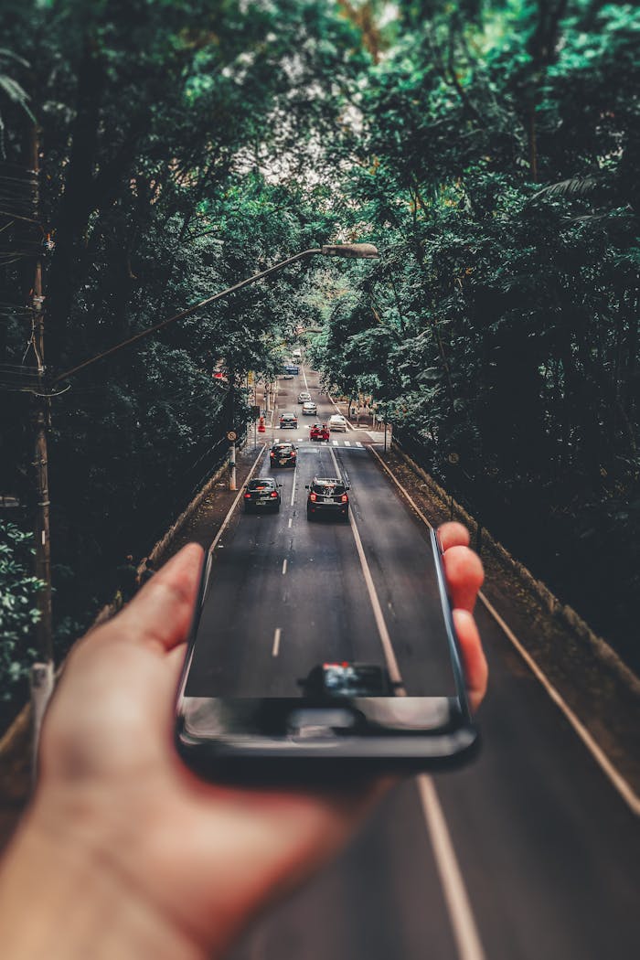 Mastering the First Impression: Your intriguing post title goes here Creative blend of technology and nature with smartphone framing a bustling road through forest.